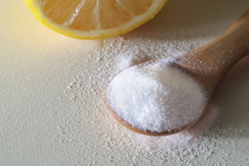 powdered Vitamin C on wooden spoon with cut lemon on white background