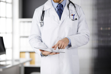 Male doctor using tablet computer in clinic, close-up. Perfect medical service in hospital. Medicine and healthcare concept