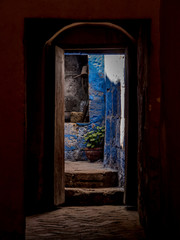 view of a ancient blue colored courtyard of Monasterio de Santa Catalina from an old wooden door. Steps in foreground. Plant pot and hob in the background. upright image