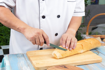 Chef holding knife cutting slide bread making on wooden board