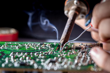 Technician repairs circuit board of television with iron soldering and tin wire, close up