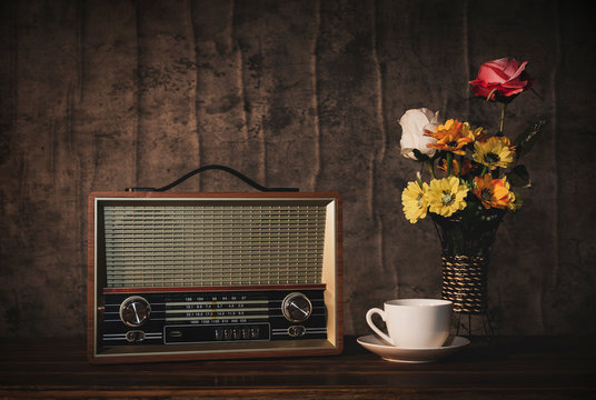 Retro old radio is still life, flower vases and white coffee cup on wooden table