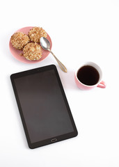 work at home with morning coffee. A tablet on a white background, next is a cup with coffee and a plate with pastries
