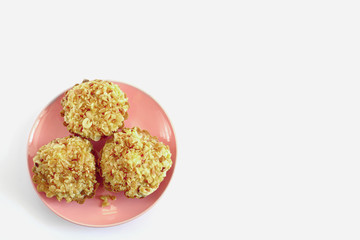 three cakes with peanuts lie on a pink plate on a white background
