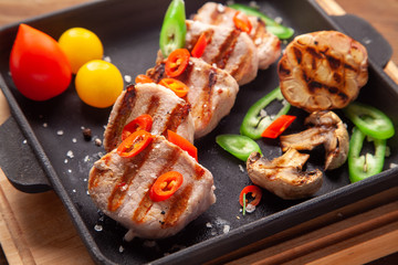 Grilled pork tenderloin  on cooking pan with tomatoes, champignons, chili peppers, sea salt