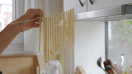 une personne fait sécher des pâtes fraiches sur un fil dans une cuisine © zoe