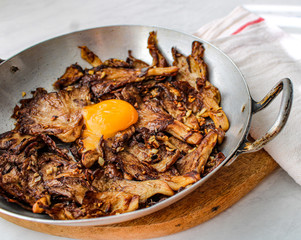 Sautéed oyster mushrooms with garlic and topped with egg yolk. Oven roasted in grey baking tray. Flat lay. Tope view. 