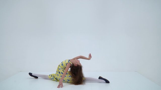 A girl in a summer dress sits on a twine on the floor