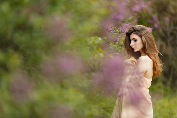 Romantic portrait of young beautiful girl standing in spring lilac garden