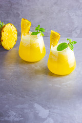 Pineapple cocktail in two glasses on a gray background. Cold pineapple cocktail with mint. Summer tropical cocktail. Healthy drink