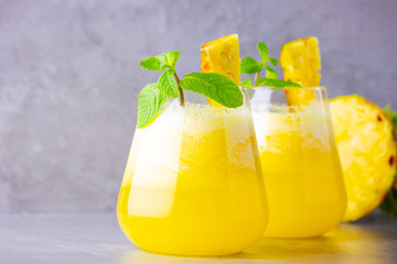 Pineapple cocktail in two glasses on a gray background. Cold pineapple cocktail with mint. Summer tropical cocktail. Healthy drink