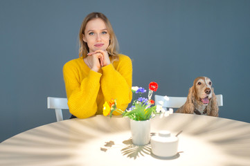 Funny portrait of blonde young girl sitting at the table with her kind cocker spaniel puppy and...