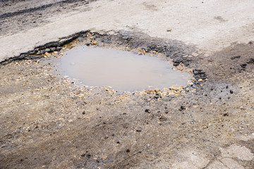 A deep hole in the road filled with water after the rain. Damaged road surface after rain.