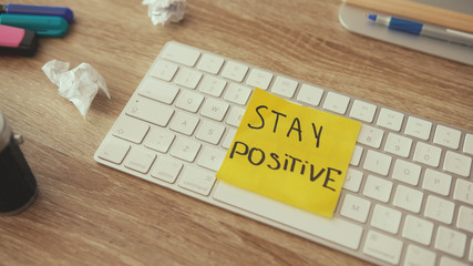 Creativity crisis and lack of ideas. Messy artist workplace desktop with crumpled paper. Man lays a positive sticker note on keyboard. Concept of motivation.