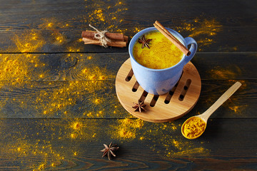 Traditional Indian drink turmeric latte or golden milk with cinnamon, star anise and turmeric on a rustic wooden table.