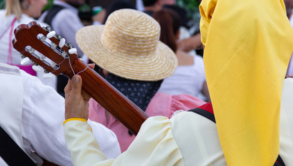 Anonymous woman playing guitar with group on traditional festival parade in Gran Canaria, Spain. Music band on street with back of lady wearing yellow head scarf. Local holiday concept