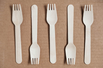 Wooden forks on a cardboard background. Eco friendly disposable tableware. Top view. Copy, empty space for text