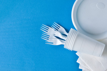 Disposable plastic tableware, forks, glasses, plates on a blue background. The problem is recycling, reuse, safe planet, environmental concept. Place for text.