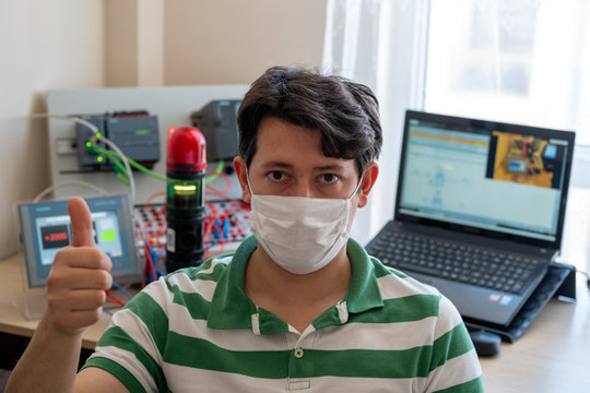 Young Man with surgical mask on face against COVID-19 ( Coronavirusis ) Working at Office and Making OK gesture at Online Education for PLC and Operator Panel Programming.