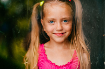 Little cute girl with blond hair and pink dress smiles behind the window