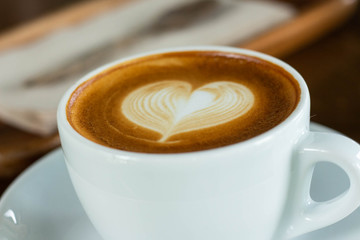 Hot coffee in a cup with foam milk beautiful art on wooden table background. Cappuccino or latte with froth foam, drinks concept.
