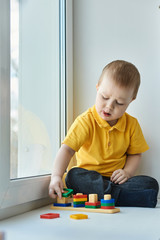 Small baby boy is sitting on windowsill, playing an educational game.