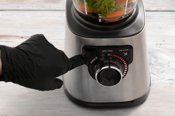 Blender, carrot, parsley, dill on a gray wooden table. Girl makes a smoothie of vegetables. Healthy...