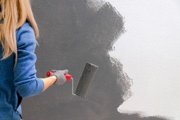 Girl holds a roller in hand close-up. Girl repaints the wall in gray. Repair in the room. DIY repair.