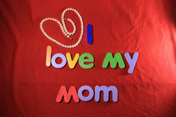 Colorful letters with I love my mom isolated on red cloth background. I love my mom spelled with colorful letters and red heart for mothers day.