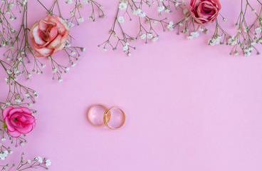 Pink rose and two golden wedding rings on pink background. Top view.