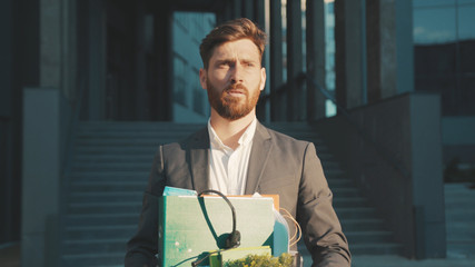 Sad office worker man walking with box of personal stuff lose a job got fired due to a coronavirus crisis unemployed depression business corporate employment economy slow motion