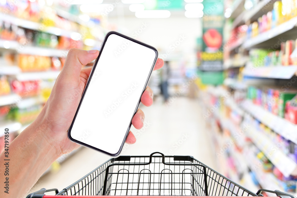 Poster Man hand holding smartphone with shopping cart in supermarket ,Empty white screen smartphone for design advertising on mobile phone screen ezy replace with clipping path