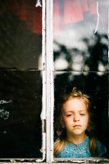 Lonely abandoned unhappy little girl looking through window with abstract reflections. Kid depressive portrait. Pathetic sad misery child eyes. Problematic childhood. Deep mood. Pensive baby face.