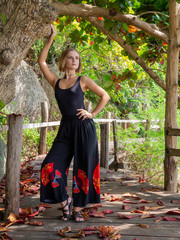 A young woman in black clothes poses by a tree in a rainforest on a wooden floor in fallen red foliage. walk in the forest on a tropical island.