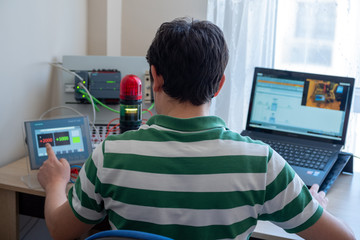 Back View of Young Man Who is Working Home Office and Making Online Education about PLC and Operator Panel Programming. Distance learning, also called distance education, e-learning or online learning