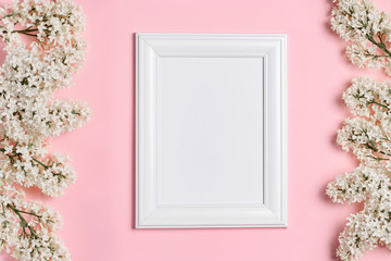 Empty white photo frame and white lilac flowers on a pink background.