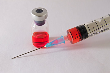 Syringe and medical vial with red liquid closeup