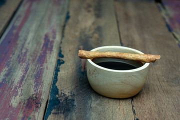 Black coffee in wooden cup with cinnamon stick on dark wooden table.