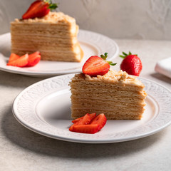 a dessert of a layer cake decorated with strawberries on a white plate on a light backdrop