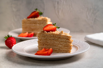 a dessert of a layer cake decorated with strawberries on a white plate on a light backdrop