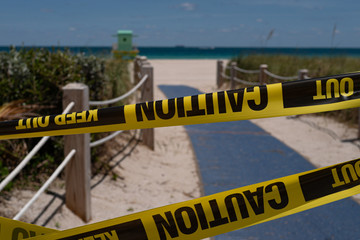Covid 19 coronaviruse disease, health risk. View from the Miami Beach beachfront to turquoise ocean with blue sky without people. Yellow Caution USA Tape of COVID-19. Coronavirus Outbreak Quarantine.