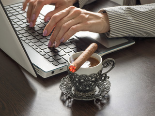 Businesswoman with a cigar is typing on a laptop keyboard