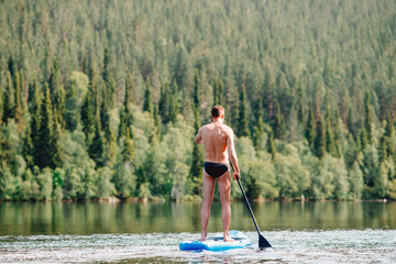 Man rowing oar on sup board blue lake water paddleboard background of forest