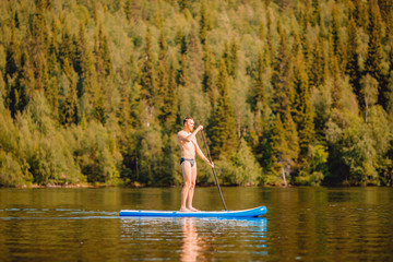 Man rowing oar on sup board blue lake water paddleboard background of forest