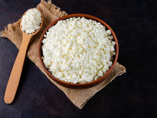 Cottage cheese on a burlap. Fresh cottage cheese and wooden spoon on a dark background. Soft cheese on a black background. Top view. Copy space