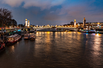 beautiful urban landscape of the seine river bordered the city of paris, in the river you can see some boats that make a house, a bridge in the distance and a sky with blue color and clouds