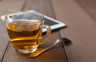 Close up hot tea cup on wood table with tea spoon and tablet shot on moning time . Soft focus and selective focus to tea cup. hot tea in glass with copy space for text or design.