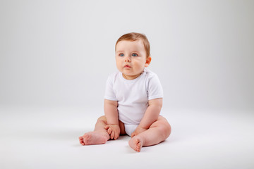 Cute toddler boy 8 months old in white bodysuit sits on white background, space for text