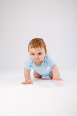 Cute toddler boy 8 months old in blue bodysuit sits on white background, space for text