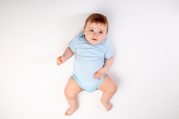Cute toddler boy 8 months old in blue bodysuit sits on white background, space for text